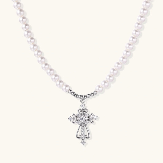 White pearl necklace with ornate silver cross pendant featuring zirconia crystals on cream background.