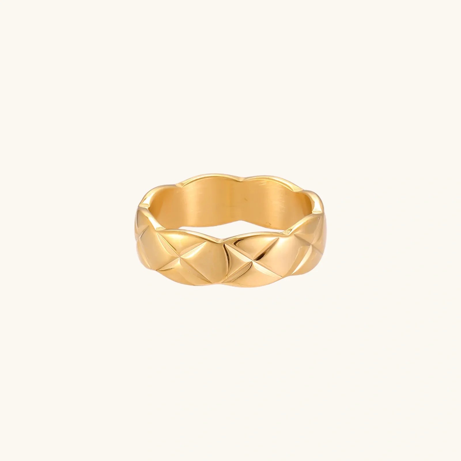 Close-up of an 18K gold-plated twisted band ring with dimensional braided pattern on cream background.